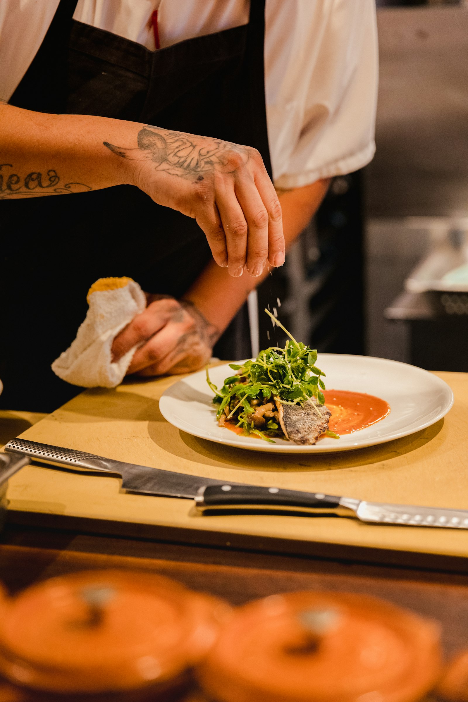 Chef carefully plating a dish with tweezers at the pass