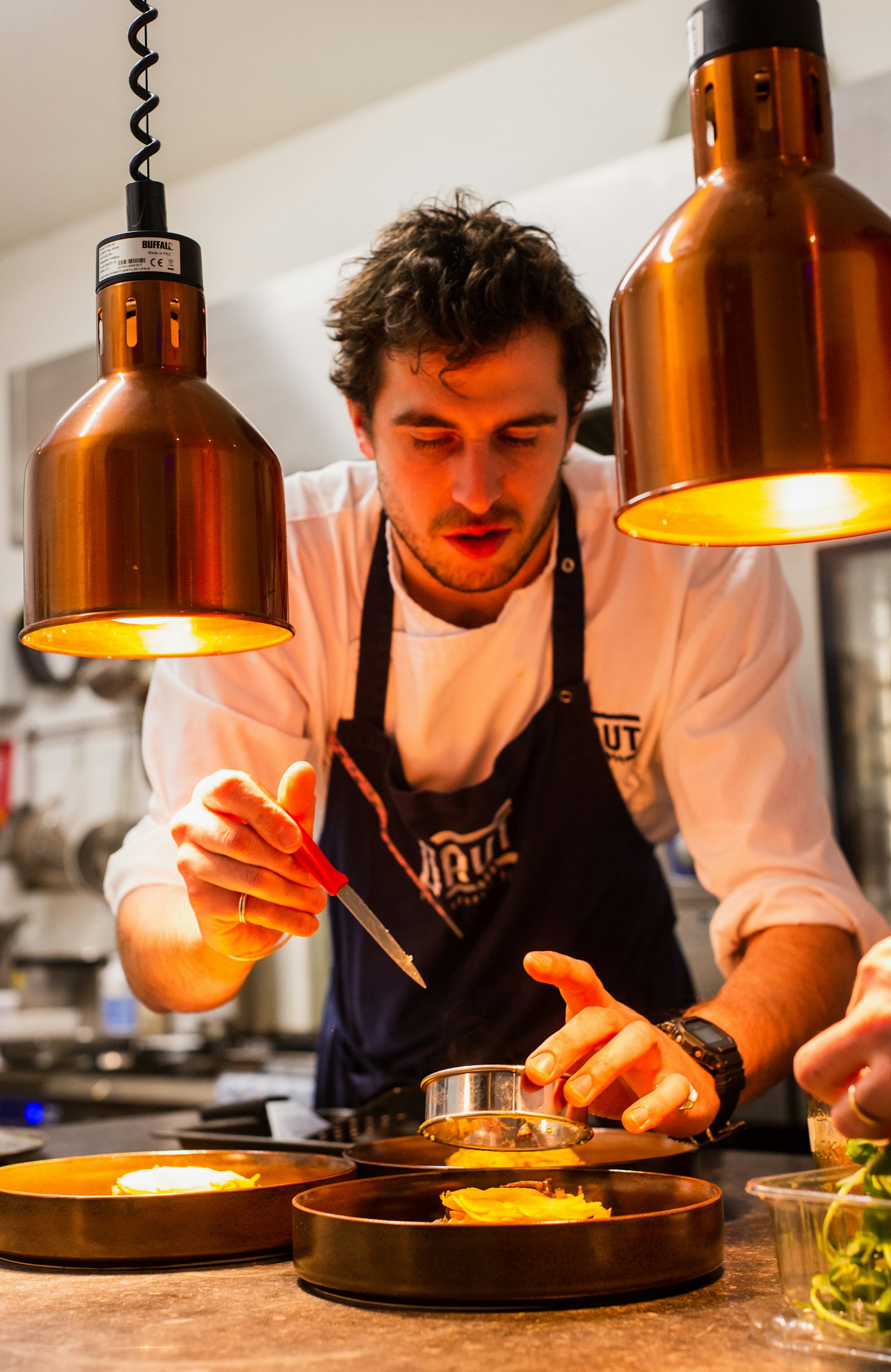 Chef in a black apron preparing food at a restaurant pass