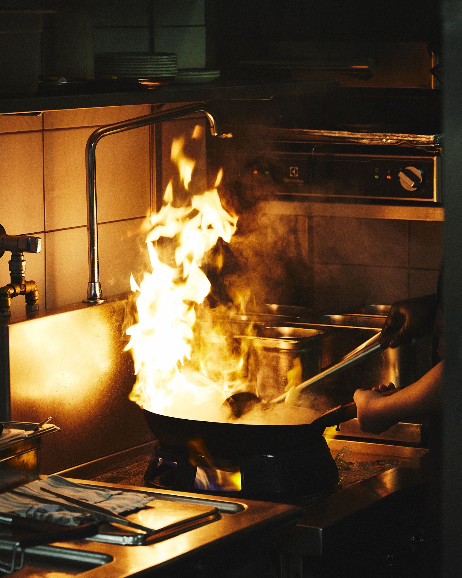 Chef managing tall flames under a wok in a professional kitchen