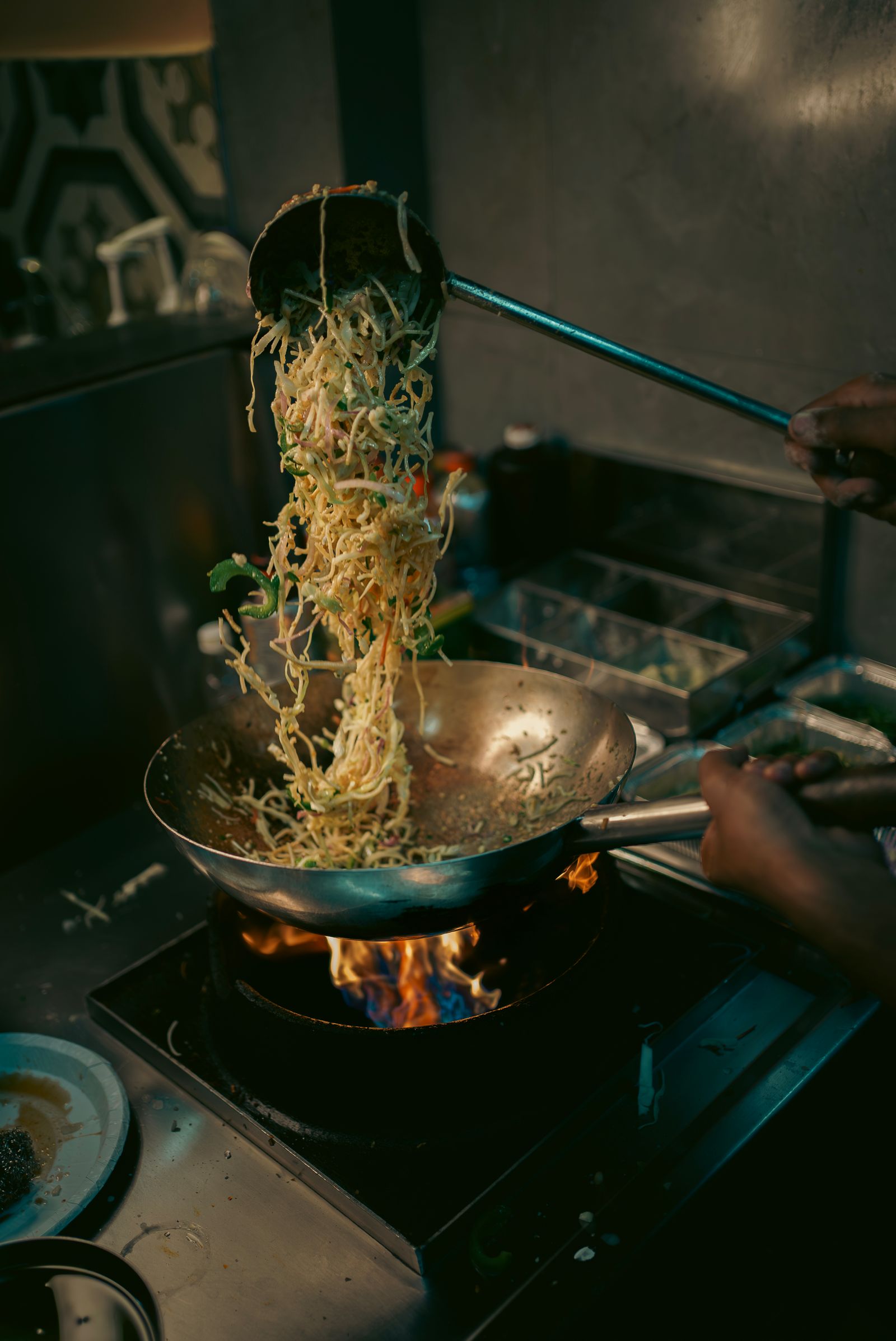 Chef tossing stir-fried noodles in a flaming wok
