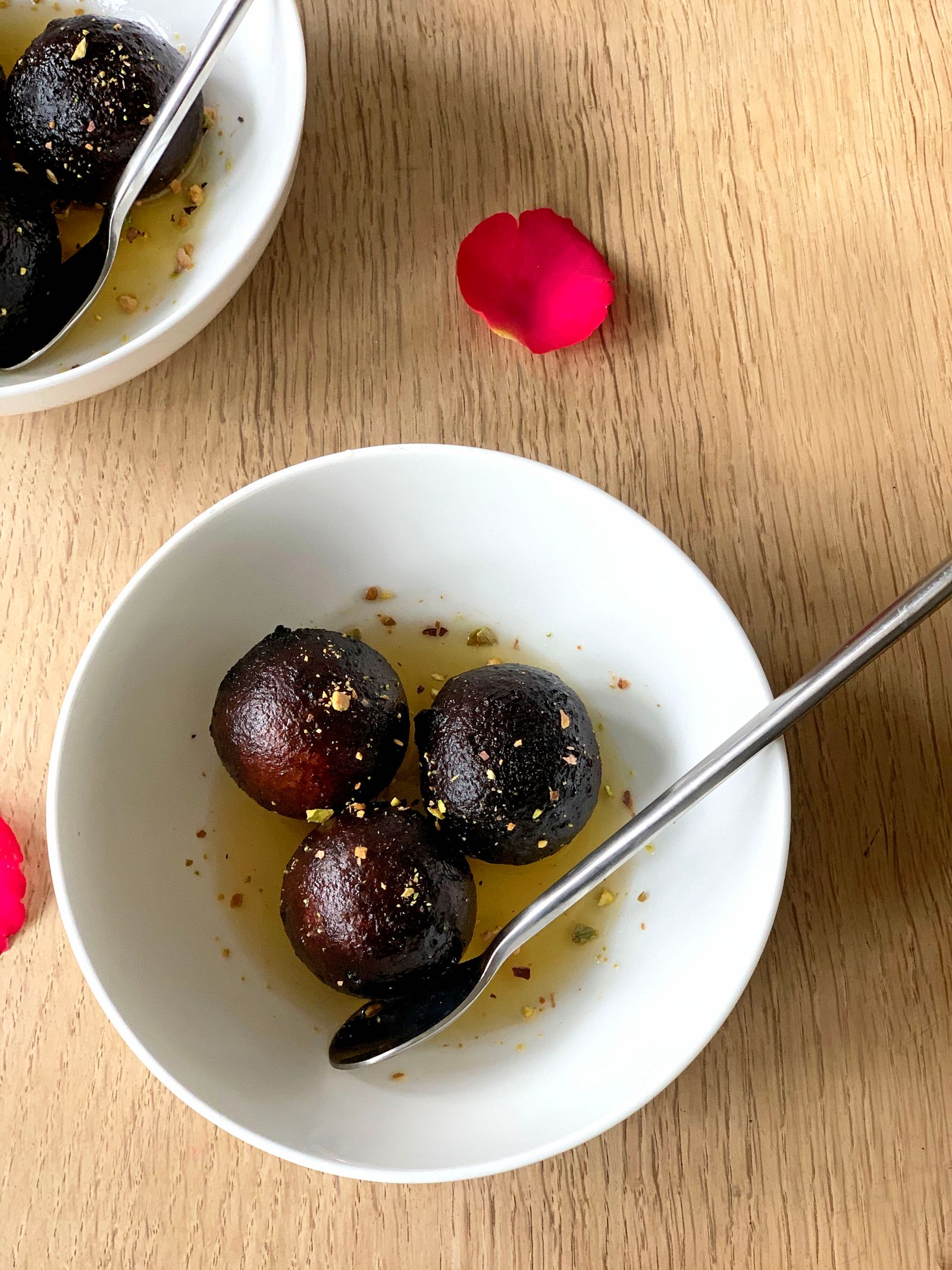 Gulab jamun with rose petals in a white bowl