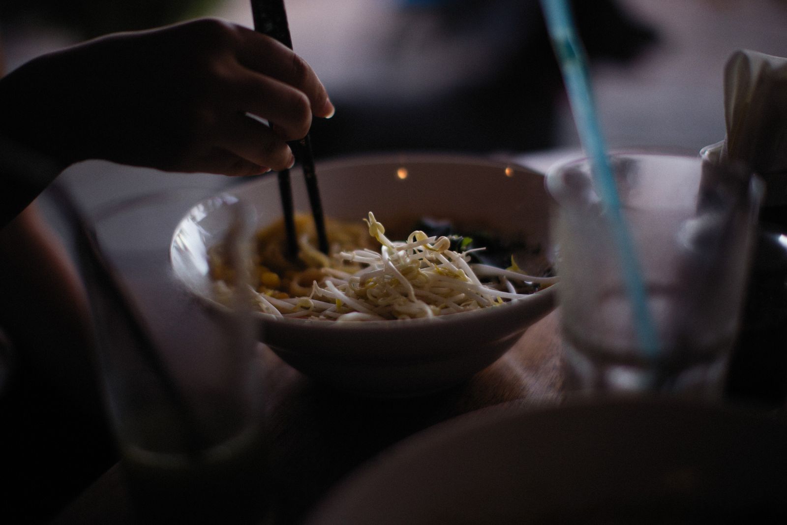 Hand lifting noodles from a bowl with chopsticks