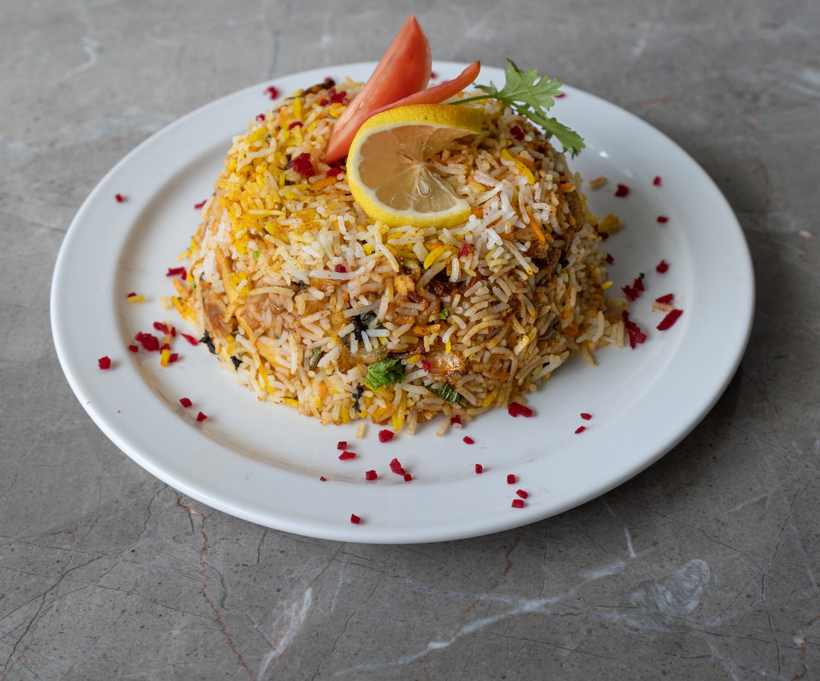 Plate of biryani garnished with lemon and tomato