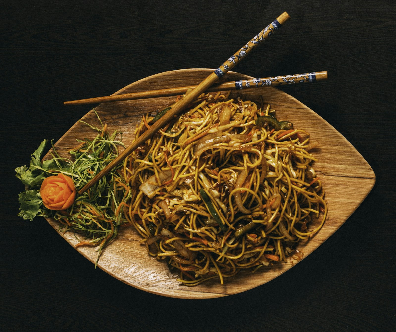 Stir-fried noodles with vegetables on a wooden platter with chopsticks