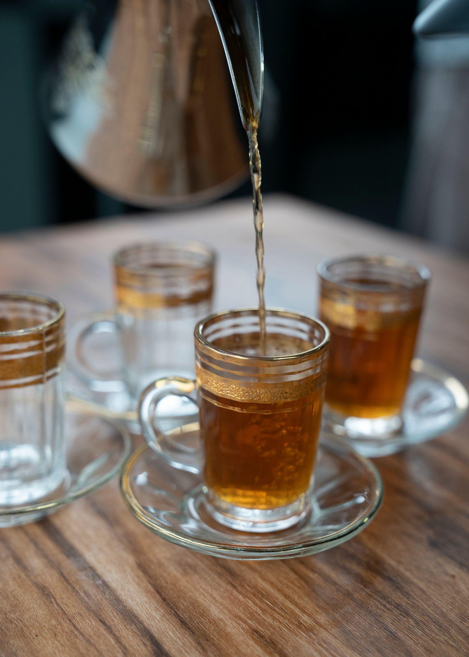 Tea being poured into glass cups on a wooden table